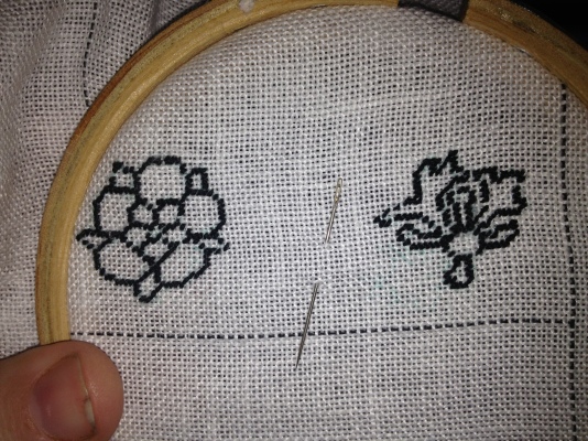 Outline of a rose (left) and incomplete outline of a honeysuckle (right) in black tent stitch.