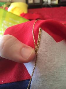 After the first cord is couched down, bend it back on itself at the point of the corner. This will result in a fold in the gold cord, and a sharper corner.